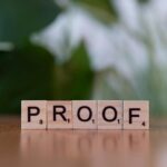 Tuiles de Scrabble en bois orthographiant « PROOF » sur une table en bois avec fond vert.