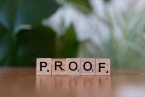 Tuiles de Scrabble en bois orthographiant « PROOF » sur une table en bois avec fond vert.