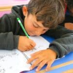 Two young boys sitting at a desk writing on paper