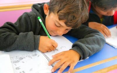Two young boys sitting at a desk writing on paper