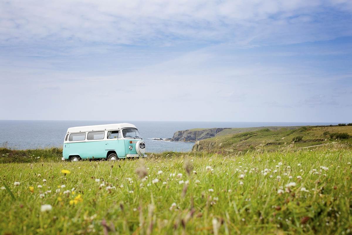 Camping-car blanc garé dans prairie fleurie face à la mer et falaises côtières