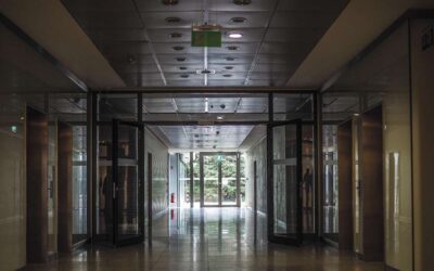 Long couloir avec portes vitrées, sol brillant, éclairage et issue vers l'extérieur