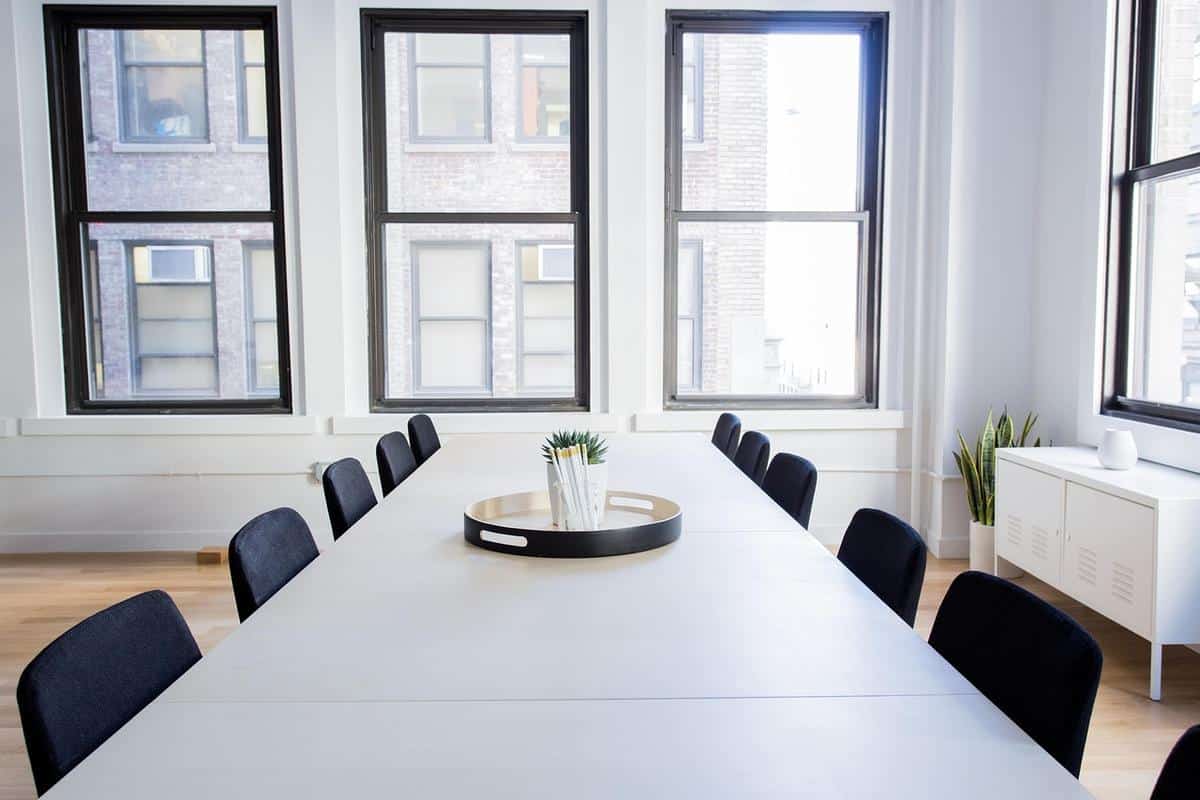 Une salle claire avec table blanche, chaises noires, grandes fenêtres et décor minimaliste